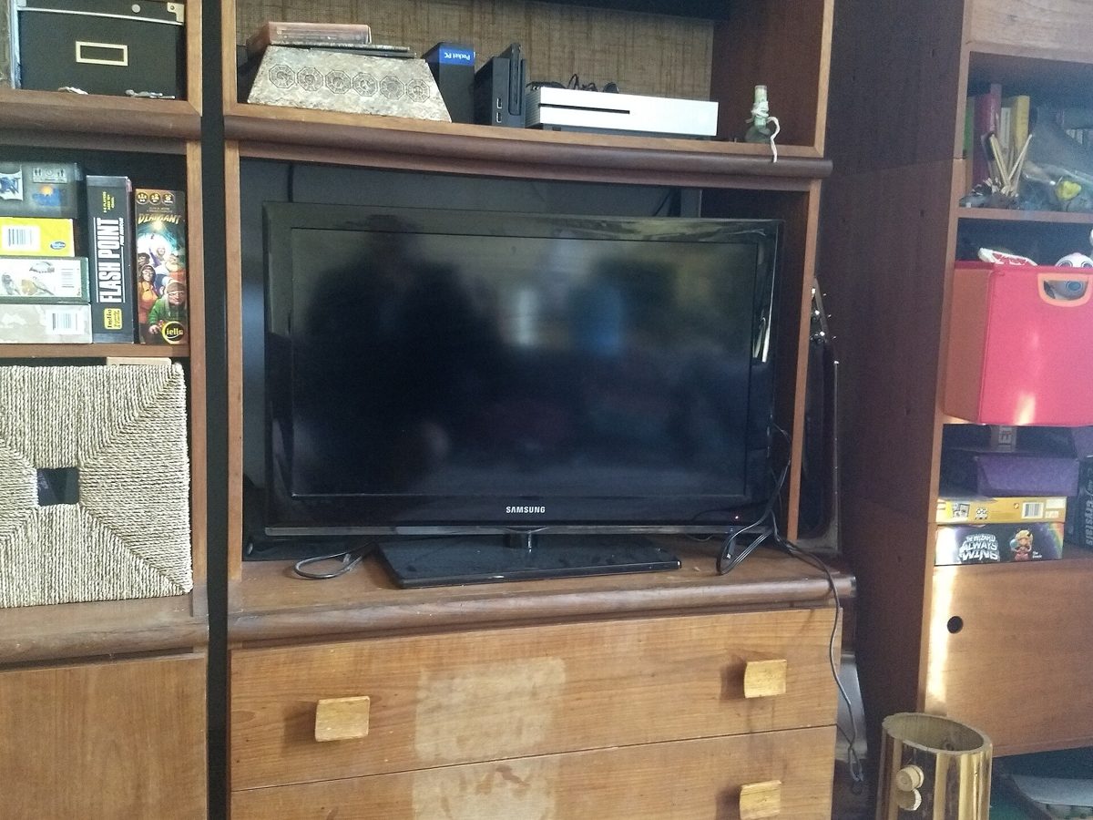 Vardagsrum med väggmonterad smart TV som visar en kanalöversikt med svenska TV-kanaler och en fjärrkontroll på soffbordet